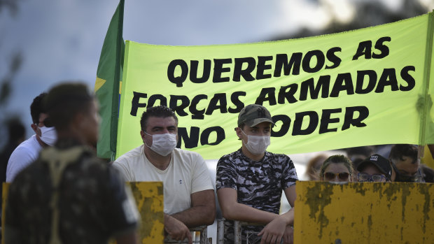 Supporters of Brazilian President Jair Bolsonaro stand with a banner that reads in Portuguese, “We want the armed forces in power,” outside his residence last year.