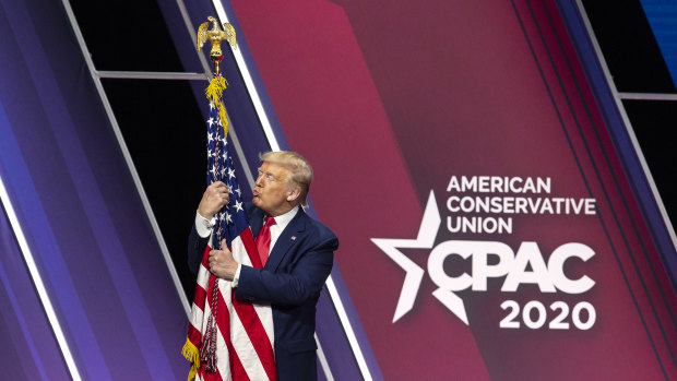 Then president Donald Trump hugs an American flag at the 2020 Conservative Political Action Conference. 
