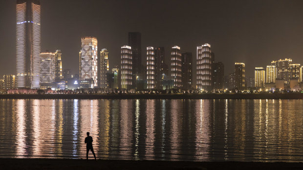 A man looks across to illuminated buildings on the other side of the Yangtze River at night in Wuhan, Hubei, China.