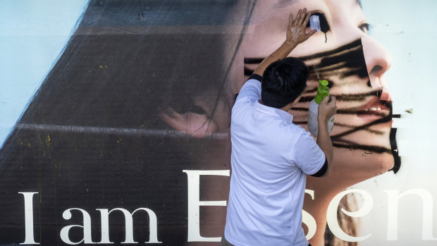 A worker cleans a spray painted mask on an advertisement at a bus station in the Central district of Hong Kong on Monday.