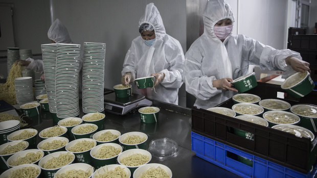 Workers wearing protective suits, masks and gloves handle containers of hot dry noodles at a noodle factory in Wuhan, Hubei Province, China.