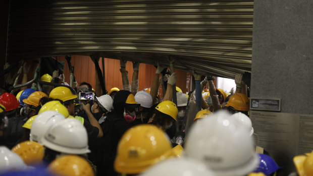 Demonstrators hold up a damaged shutter after breaking into the Legislative Council building.