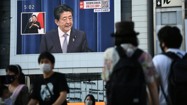 Pedestrians walk past a screen displaying a live broadcast of Prime Minister Shinzo Abe speaking on Friday. 