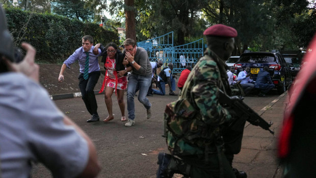 Pedestrians flee the hotel and office complex as a member of the security forces watches during an attack in the Westlands district.