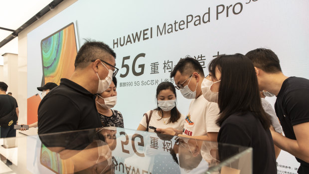 Customers wearing protective masks stand in front of an advertisement for Huawei.