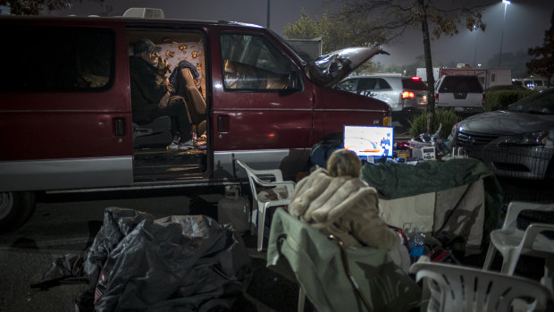 A Camp Fire evacuee plays with a dog in a vehicle, left, while a woman watches television as they camp in a Walmart Inc. store parking lot in Chico, California.