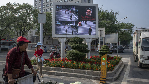 At a crossroad equipped with monitoring cameras linked to facial recognition technology, a screen displays photos of jaywalkers alongside their name and identification number in Xiangyang, China.