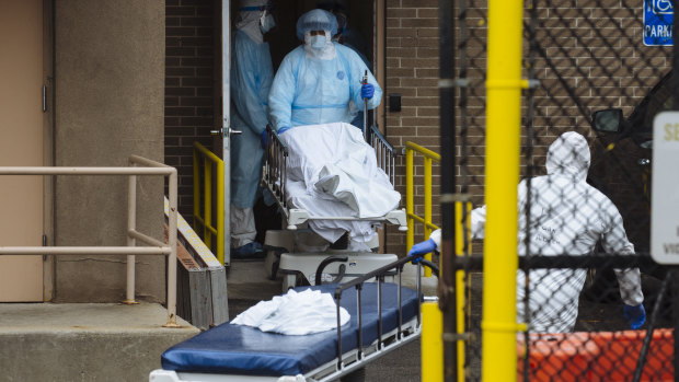 Medical workers in protective clothing move the body of a deceased patient to a refrigerated overflow morgue outside the Wyckoff Heights Medical Centre in Brooklyn, New York.