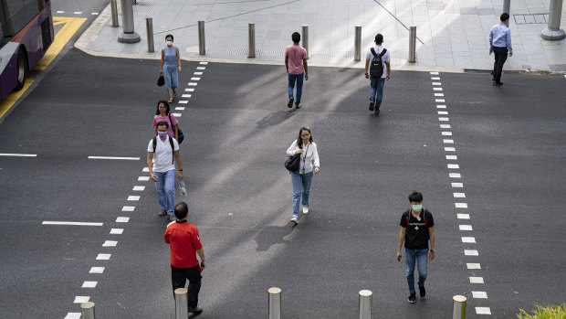 People keep their distance while crossing a road in Singapore to curb the spread of COVID-19.