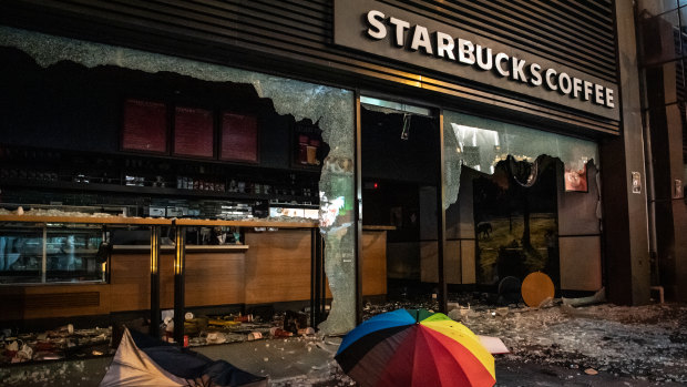 A coloured umbrella and debris lie outside a vandalized Starbucks.
