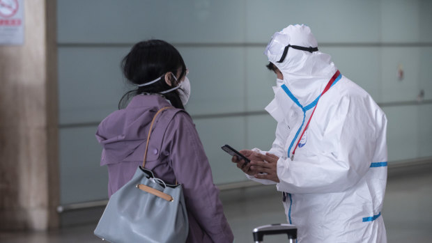 China's early, tough measures have been a success ... an airport employee wearing a full-body protective suit assists a traveller at the Capital International Airport in Beijing this week.