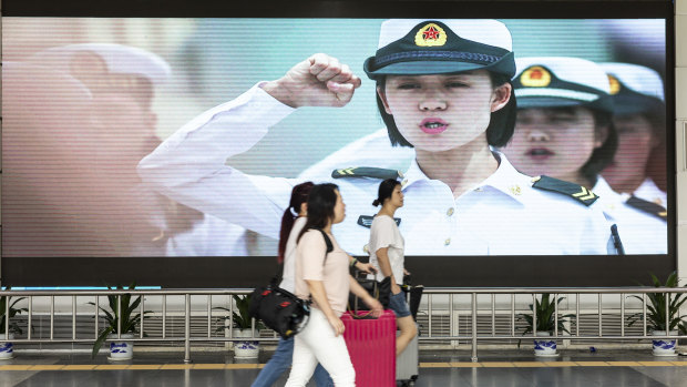 Travellers walk past an advertisement for the People's Liberation Army (PLA) on a screen near the Luohu border crossing in Shenzhen, China.