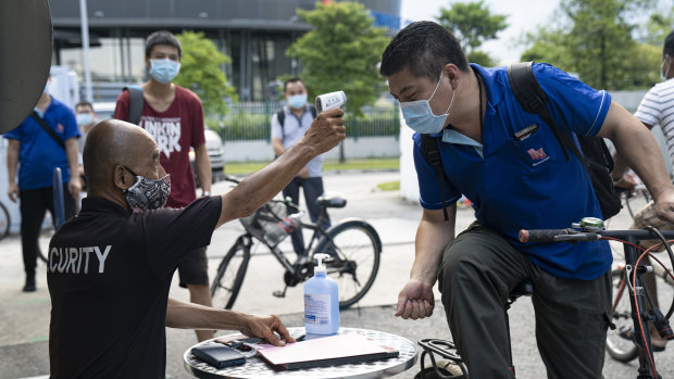 A migrant worker wearing protective face mask has his temperature checked by a security guard before entering a factory-converted dormitory.