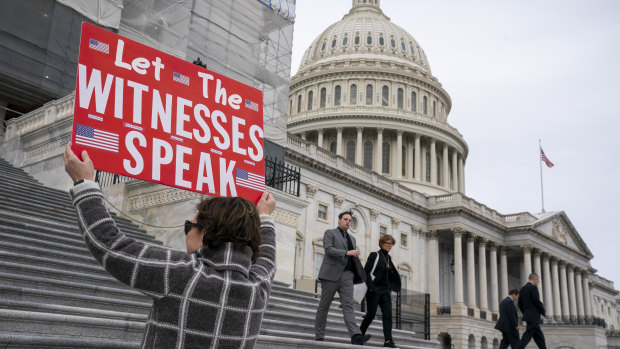 A protester displays a message for members of the House as they leave the Capitol in Washington on Friday.  The House wants more witnesses to testify in Trump's Senate impeachment trial.