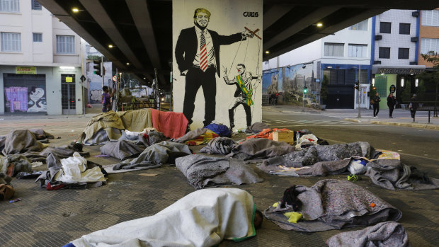 Homeless people sleep under a bridge in front of a mural depicting US President Donald Trump as a puppeteer manipulating Brazil's President Jair Bolsonaro, in downtown Sao Paulo, Brazil.