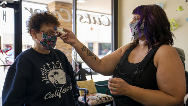 A hair stylist wearing a protective mask checks a customer's temperature at a hair salon in Mustang, Oklahoma. 