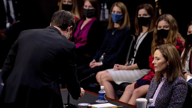 Supreme Court nominee Amy Coney Barrett watches as an aide tests her microphone during a confirmation hearing before the Senate Judiciary Committee.