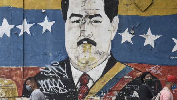 Pedestrians wearing protective masks walk by a mural of President Nicolas Maduro in Caracas, Venezuela, on Tuesday.