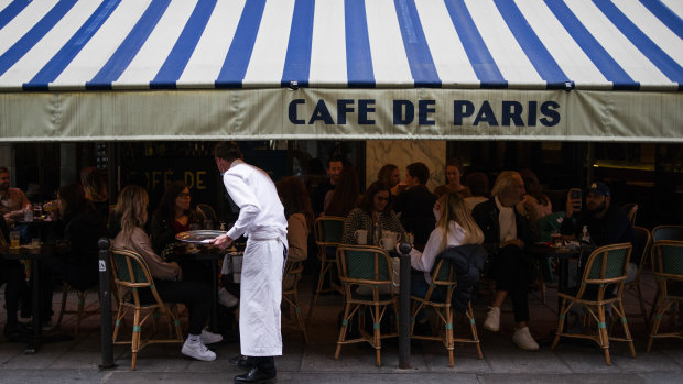 A waiter serves customers eating and drinking on the terrace area outside Cafe de Paris, ahead of the enforcement of new Covid-19 restrictions which will see bars and restaurants closing early, in Paris.
