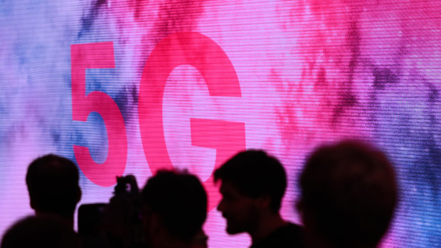 Attendees are silhouetted beside a 5G display on the Deutsche Telekom exhibit in Berlin.