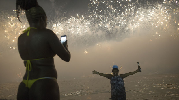 A woman poses for a picture as the fireworks explode over Copacabana Beach.