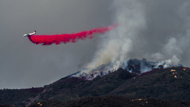 A plane drops fire retardant as firefighters continue to battle a wildfire in the Cleveland National Forest near Corona, California.