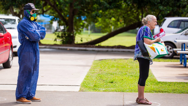 A voter wearing a protective suit and a gas mask stands spaced apart behind another voter outside a polling station during the local government elections in Noosa.