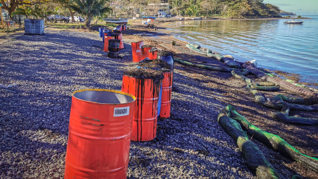Drums filled with fuel oil waste and algae sit behind foam-filled oil containment booms on shore at Bois des Amourettes, Mauritius.