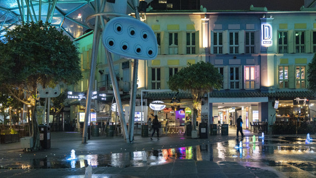 People walk past nearly empty restaurants in Clarke Quay in Singapore. 