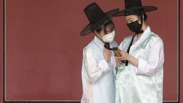 Women in traditional clothing and face masks look at a mobile phone at the Gyeongbok Palace, one of South Korea’s well-known landmarks, in Seoul.