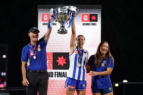 Darren Crocker, Senior Coach of the Kangaroos, Jasmine Garner of the Kangaroos and Nicole Bresnehan of the Kangaroos hold the Premiership Cup aloft.