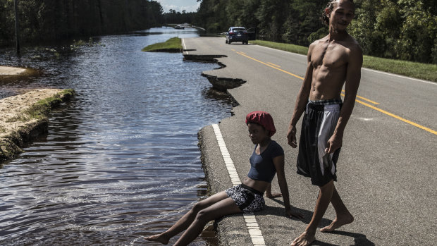 A woman sits on a damaged road surrounded by floodwaters in Currie, North Carolina.