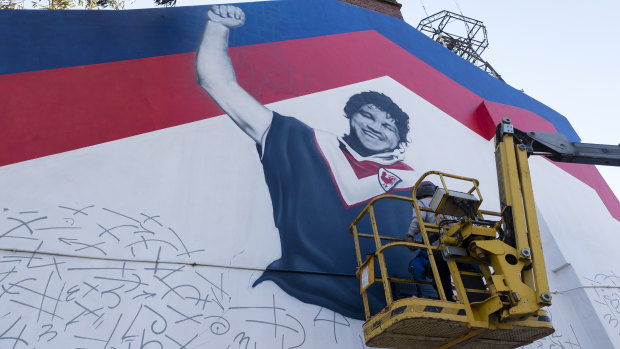 Artist Sid Tapia paints a Roosters mural including Arthur Beetson onto a Waverley home on Thursday.