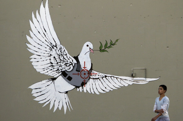 A Palestinian youth walks past the painting of a dove of peace wearing a flak-jacket which is widely attributed to Banksy on a wall in the West Bank town of Bethlehem. 