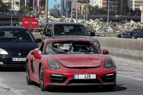 A driver wearing a protective face mask drives a badly damaged Porsche SE luxury automobile in Beirut, Lebanon, on Wednesday.