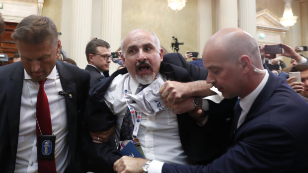 A journalist is removed from the room for trying to stage a protest.