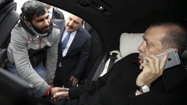Recep Tayyip Erdogan holds a citizen by the hand while speaking on his iPhone in 2015. He is now calling for a boycott of American products, including the iPhone.