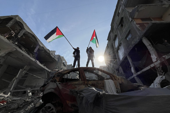 Two children wave Palestinian flags on a wrecked car as displaced Palestinians start to return to Beit Lahiya and Jabaliya.