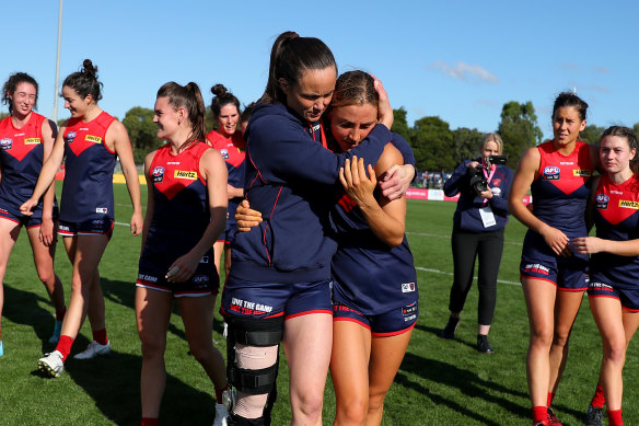 Daisy Pearce, wearing a leg brace, hugs teammate Eliza McNamara after the Demons defeated the Lions.