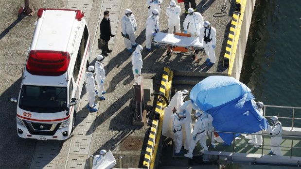 Medical workers in protective suits lead a passenger who tested positive for coronavirus from the Diamond Princess in Japan.