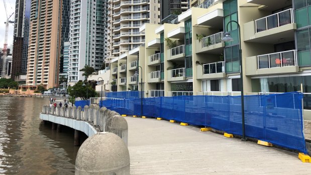 Repairs are needed along a stretch of the Brisbane City Council-managed riverwalk under large planter boxes between the riverwalk and an apartment building behind it.