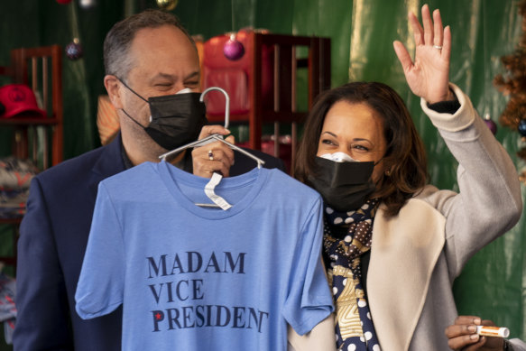 Vice President-elect Kamala Harris, accompanied by her husband Doug Emhoff, left, holds up a T-shirt as they visit the “made in DC” booth in the Downtown Holiday Market in Washington.