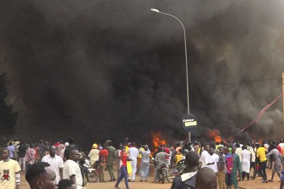 With the headquarters of the ruling party burning in the back, supporters of mutinous soldiers demo<em></em>nstrate in Niamey.