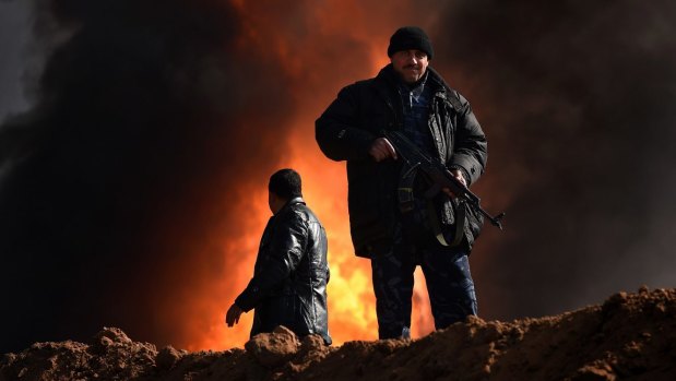 Two men provide security in the Qayyarah oil fields where ISIS set fire to wells when it retreated, sending plumes of toxic black and white smoke that blanket the sky.
