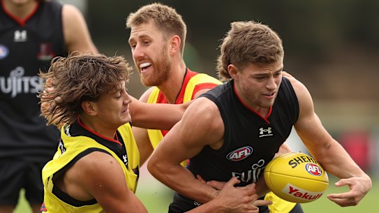 MELBOURNE, AUSTRALIA - MAY 19: Brayden Ham of the Bombers is challenged by Tex Wanganeen and Dyson Heppell during an Essendon Bombers AFL training session at The Hangar on May 19, 2022 in Melbourne, Australia. (Photo by Robert Cianflone/Getty Images)