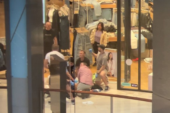 An injured person on the ground is assisted by members of the public, including Reid (in the black shirt) inside the shopping centre.