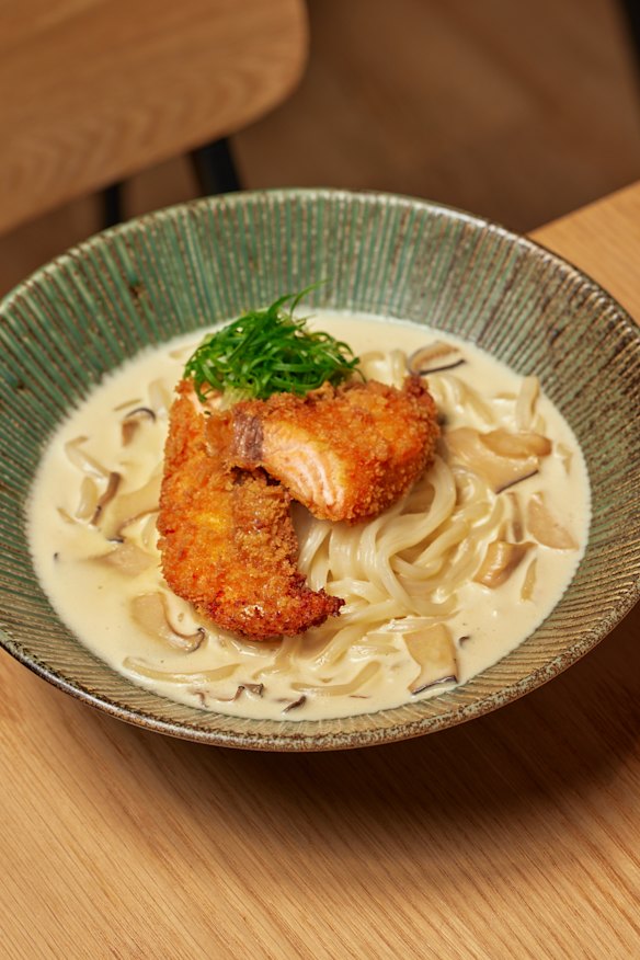 Crispy breaded salmon sits atop carbonara-style udon.