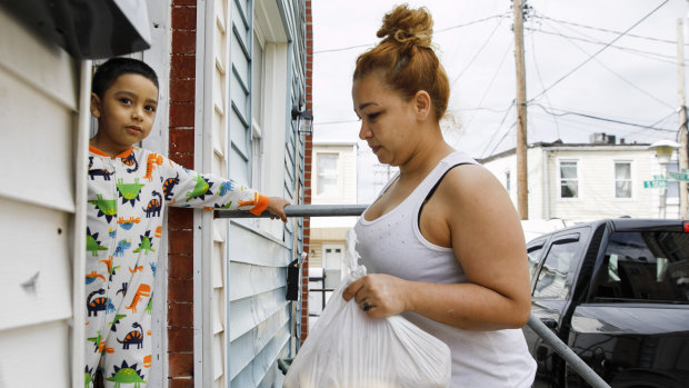 A family beset by food insecurity as coronavirus hits in Baltimore. A boy stands in the doorway as his mother carries in a bag of food brought to their home.