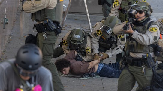 A Sheriff deputy takes aim at a photographer as deputies wrestle protesters to the ground after shooting them with less-than-lethal weapons at close range in Los Angeles.