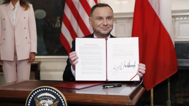 Polish President Andrzej Duda holds up an agreement signed with Donald Trump in the Diplomatic Reception Room of the White House.